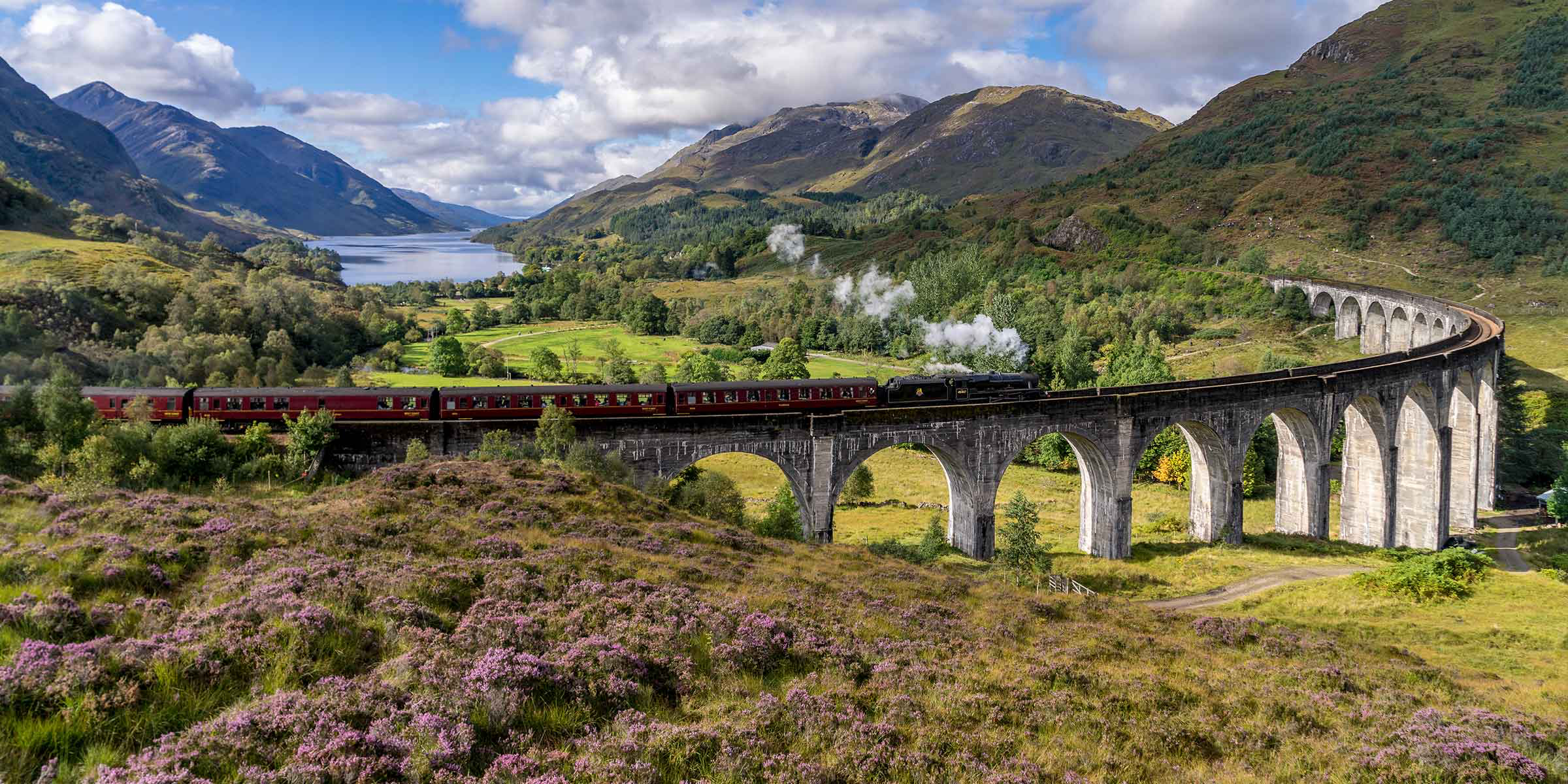 A steam train crossing Glenfinnan Viaduct with Loch Shiel and the surrounding hills beyond