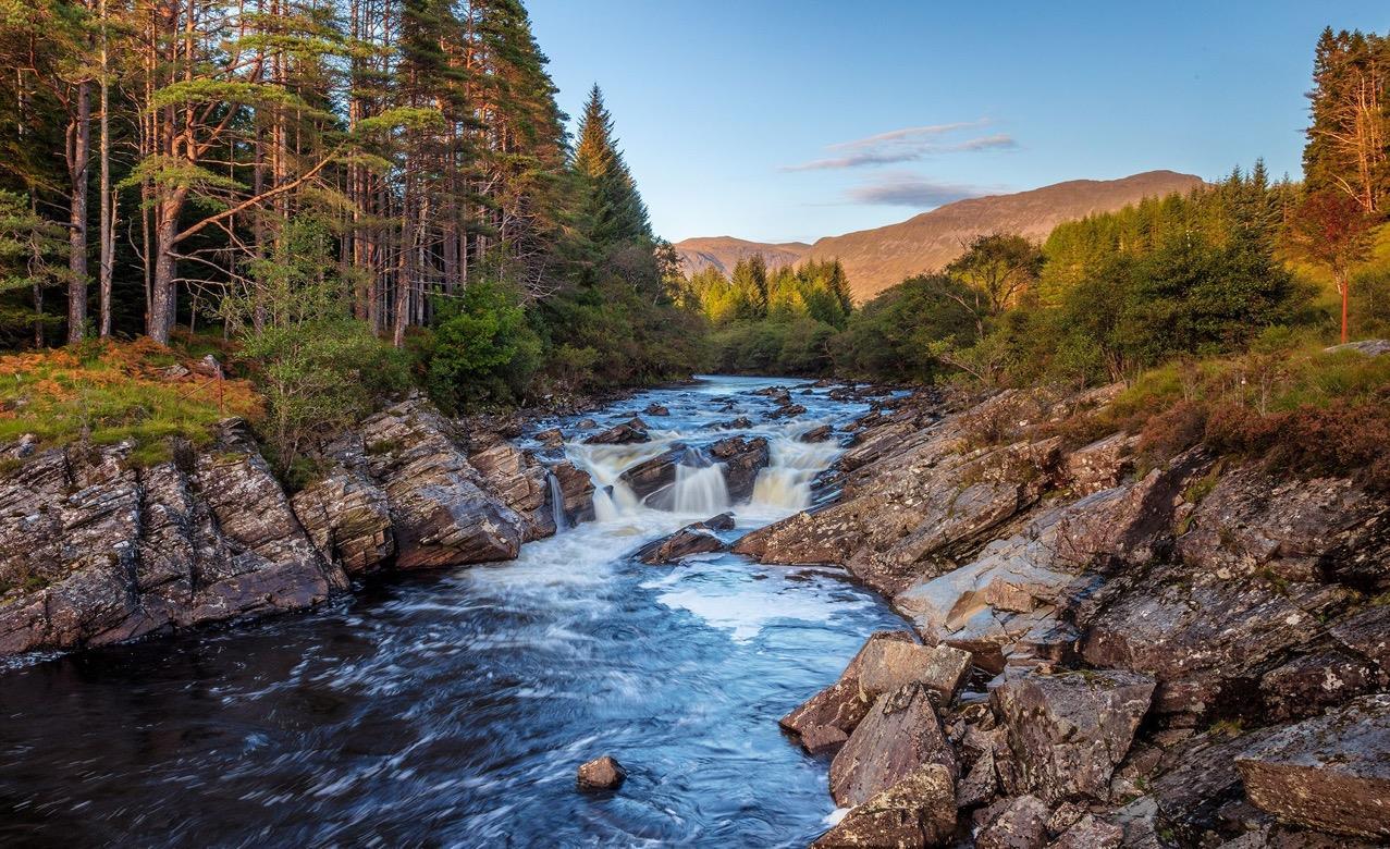 A Highland river running through woodland beneath the mountains